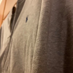 Grå hoodie från Ralph Lauren - Säljer en stilren grå hoodie från Ralph Lauren med dragkedja. Perfekt för en avslappnad look. Hoodien har långa ärmar och en mjuk insida.