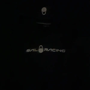 Svart hoodie från Sail Racing - Snygg svart hoodie från Sail Racing med vit logga på bröstet och på luvan. Perfekt för en avslappnad stil. Den har en klassisk passform och är tillverkad i ett mjukt material för extra komfort. 