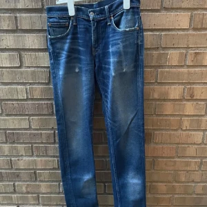 Levis jeans - Snygga blå jeansbyxor med en klassisk femficksdesign och slitna detaljer. De har en knappgylf och är perfekta för en avslappnad stil. Passformen är smal och de har en lätt tvättad look som ger en trendig känsla.