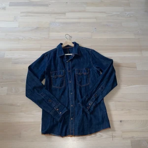 Jeansskjorta från Nudie  - Snygg jeansskjorta från Nudie Jeans i mörkblå denim. Den är i storlek M men sitter nog mer mot L. Den är i sjukt bra skick och knappt använd.