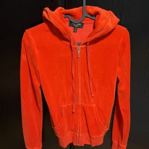 Röd velour hoodie från Juicy Couture - Säljer en snygg röd velour hoodie från Juicy Couture. Den har dragkedja framtill och en mysig huva med knytband. Perfekt för en avslappnad stil. Två praktiska fickor framtill.