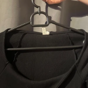 Svart ribbad klänning från H&M - Snygg svart ribbad klänning från H&M med långärmad design. Perfekt för en stilren look. Klänningen har en enkel och elegant passform som framhäver figuren.