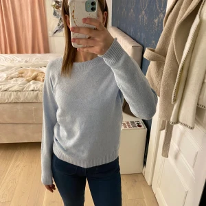 Ljusblå stickad tröja från VeroModa  - Säljer en ljusblå stickad tröja med rund hals och långa ärmar. Perfekt för kyligare dagar och lätt att matcha med olika outfits. Tröjan har ribbade muddar vid ärmslut och nederkant.