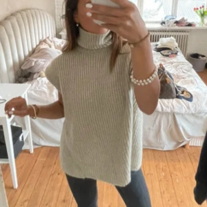 Beige stickad polotröja från Zara - Säljer en beige stickad polotröja från Zara med en unik öppen ryggdesign. Tröjan är ärmlös och har en hög polokrage som ger en stilren look. Perfekt för lager-på-lager under kyligare dagar. Passar bra till både jeans och kjol för en trendig outfit.