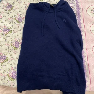 Mörkblå hoodie från Bvaldi - Säljer en snygg mörkblå hoodie från Bvaldi i en mjuk blandning av merinoull och kashmir. Tröjan har en klassisk design med dragsko i huvan och ribbade muddar. Perfekt för kyliga dagar!