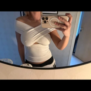 Vit omlott topp - Säljer en stilren vit omlott topp med offshoulder-design. Toppen har en tight passform och är perfekt för en trendig look. Den är tillverkad i ett mjukt och bekvämt material.