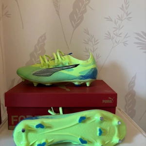 Neongröna fotbollsskor från Puma - Snygga neongröna fotbollsskor från Puma med blå och svarta detaljer. Skorna har snörning och dobbar för optimalt grepp på planen. Perfekta för den som vill sticka ut på fotbollsplanen. Storlek 44! Helt nya! Skick 10/10 aldrig använda! SG dobb på så bara för den som tränar/spelar på gräs!