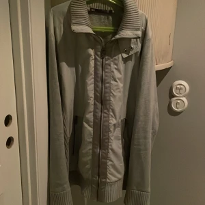 Grå jacka från WE - Säljer en stilren grå jacka från WE med dragkedja och ribbad krage. Jackan har långa ärmar och ribbade muddar, vilket ger en skön passform. Perfekt för kyligare dagar!