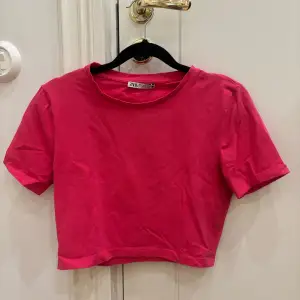 Säljer en snygg rosa croppad t-shirt från Zara. Den har korta ärmar och är perfekt för en avslappnad stil. Gjord i mjukt bomullsmaterial för extra komfort.