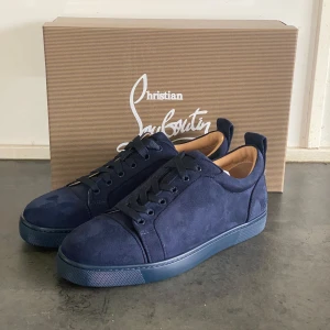 Christian Louboutin Mörkblå - Snygga mörkblå sneakers från Christian Louboutin i mocka med den ikoniska röda sulan. Skorna har snörning och en stilren design som passar perfekt för en trendig look. Levereras med originalförpackning och dustbag. Finns inte din storlek? Vi kan fixa alla storlekar bara att höra av sig så löser vi de du vill ha! Vi kan även fixa alla skor, tröjor, jackor, västar osv till riktigt bra pris bara att skicka bild på vad du söker och storlek så ska vi göra de vi kan!/// Es Clothing