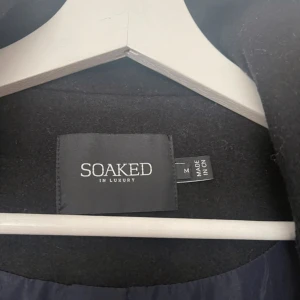 Svart kappa från Soaked in Luxury - Elegant svart kappa från Soaked in Luxury i storlek M. Kappan har en stilren design med långa ärmar och en diskret dragkedja framtill. Perfekt för kyligare dagar med sitt mjuka och bekväma material.