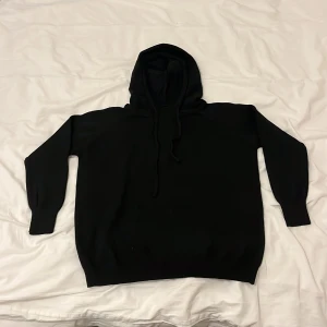 Svart merinoull hoodie - Säljer en klassisk svart hoodie med långa ärmar och ribbade muddar. Perfekt för en avslappnad stil och enkel att matcha med andra plagg. Huvan har dragsko för justerbar passform.