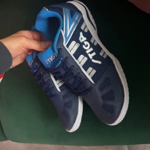 Blå pingis/badminton skor från Stiga - Snygga blå sneakers från Stiga med vita detaljer och snörning. Skorna har en sportig design med mönstrad sula för bra grepp. Perfekta för träning eller vardagsbruk.