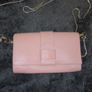 Kall-rosa axelremsväska - Snygg rosa axelremsväska med kedja och flera fack för kort och annat. Den har en stilren design och är från Saddler. Gjord av läder. 