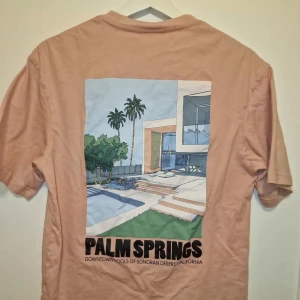 Rosa t-shirt med Palm Springs-tryck från H&M - Snygg rosa t-shirt från H&M med ett coolt Palm Springs-tryck på både fram- och baksidan. Perfekt för en avslappnad stil.