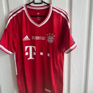 Bayern München finaltröja 2013 Ribéry - Röd Bayern München fotbollströja från Adidas med vita detaljer, Champions League-final Wembley 2013-tryck och Ribéry 7 på ryggen. Broderad klubbmärke och stjärnor på bröstet, kortärmad modell med V-ringning.