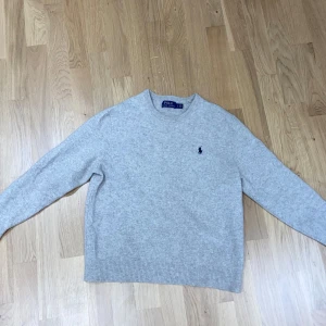 Beige stickad tröja från Polo Ralph Lauren - Säljer en klassisk beige stickad tröja från Polo Ralph Lauren med rund halsringning och diskret broderad logga på bröstet. Perfekt för en stilren och enkel look. 