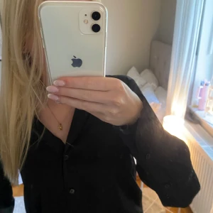 Svart skjorta från H&M - Säljer en svart skjorta från H&M i storlek XS. Skjortan har klassisk krage, knäppning framtill med svarta knappar och långa ärmar. Perfekt att styla till olika outfits. Materialet känns mjukt och lätt mot huden.