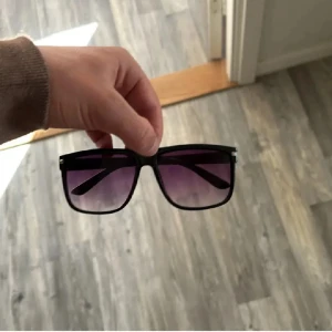 Likande raybans boyfriend  - Stilrena svarta solglasögon med fyrkantig oversized båge och tonade glas i lila till transparent. Perfekta för att lyfta din look med en modern touch. Bågarna är i plast och har en klassisk design.