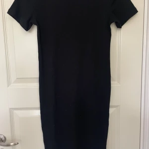 Svart ribbad kortärmad klänning - En svart ribbad klänning med kort ärm och rak passform. Materialet är stretchigt och bekvämt.