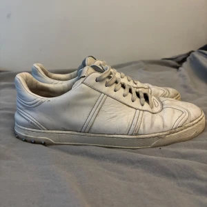 Vita sneakers Valentino - Säljer ett par vita sneakers från Valentino med klassisk design och rund tå. Skorna är i skinn och har platt sula med små nitar baktill. Perfekta för dig som gillar stilrena och exklusiva sneakers. Många nitar kvar. Skick 5/10. 