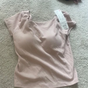 Ljusrosa ribbad topp med inbyggd bh från Uniqlo - Säljer en ljusrosa ribbad topp från Uniqlo Airism-kollektionen. Toppen har korta ärmar och en fin ringning. Materialet är mjukt och stretchigt, perfekt för varma dagar. Toppen tillhör deras kollektion ”bra tops” och har en bekväm inbyggd bh. Min syster köpte den här toppen i Thailand. Enligt lappen är storleken M, men jag som passar i S/XS skulle säga att den passar utmärkt. 