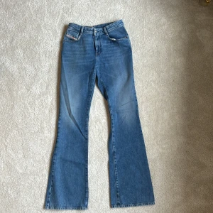 Blå bootcut jeans från Diesel - Säljer ett par klassiska blå bootcut jeans från Diesel med fem fickor och snygga detaljer. Jeansen har hög midja och är tillverkade i bomull. Perfekta för dig som gillar en tidlös och avslappnad stil.
