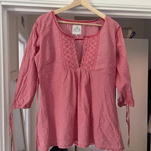 Röd- och vitmönstrad blus från ZE ZE - Säljer en röd- och vitmönstrad blus från ZE ZE med broderade detaljer och knappar framtill. Den översta knappen saknas tyvärr. Blusen har trekvartsärm med knytband och ett diskret rutigt mönster. Perfekt för dig som gillar bohemisk stil!