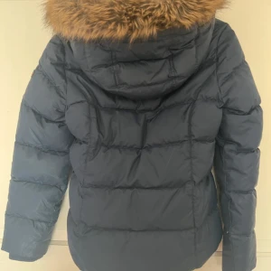 Blå dunjacka med fuskpäls från Tommy Hilfiger - Mörkblå dunjacka med huva. Jättesköna jacka och bra skick. Tveka inte att skriv ell fråga💕