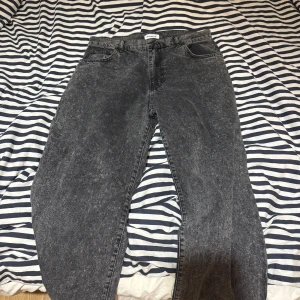 Mörkgrå jeansbyxor från Woodbird - Säljer ett par mörkgrå jeansbyxor från Woodbird i tvättad look. Byxorna har klassisk femficksdesign, normal passform och raka ben. Perfekta för dig som gillar en avslappnad stil med lite vintagekänsla.