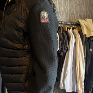 Cardigan/jacka från Parajumpers - Säljer en svart jacka/cardigan från Parajumpers. Västen har dragkedja framtill och ett märke på ärmen. Snygg och sportig design med detaljer i orange. Jätteskön till våren och hösten eller bara dn sen sommarkväll. Den är använd ca 2 gånger och har inga defekter! 