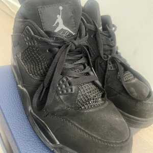 Svarta Nike Air Jordans sneakers - Säljer ett par helsvarta Nike Air Jordans med klassisk Jumpman-logga på plös och häl. Skorna har snörning, meshpaneler på sidorna och en robust sula. Perfekta för dig som gillar streetwear och vill ha en ikonisk sneaker i garderoben.