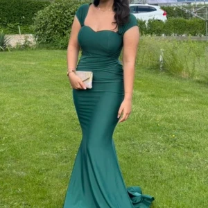 Grön långklänning med sweetheart-urringning - Säljer en elegant grön långklänning med figurnära passform och sweetheart-urringning. Klänningen har breda axelband och markerad midja som framhäver siluetten. Perfekt för bal eller festliga tillfällen.