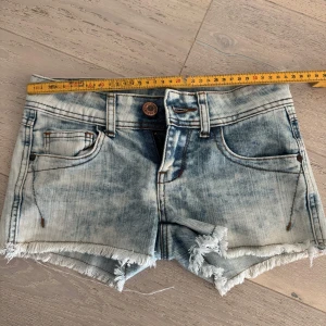 Lågmidjade ljusblå jeansshorts Tally Weijl - Säljer ett par ljusblå jeansshorts från Tally Weijl med slitna kanter. Shortsen har låg midja. Superfina till sommaren. Tyvärr lite för små för mig. Mått i midjan 34 cm som ni ser på första bilden.