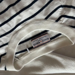 stickad topp  - Säljer en vit stickad topp med marinblå/svarta  ränder från Holly & White. Tröjan har rund halsringning och korta ärmar. Perfekt nu till sommaren!! Tröjan är inte speciellt använd och har inte något synligt fel, nyttskick.