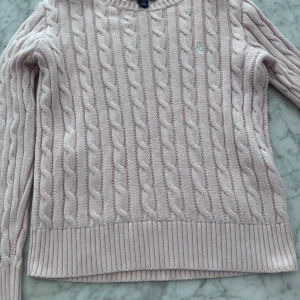 Ljusrosa kabelstickad tröja från Polo Ralph Lauren - Säljer en ljusrosa kabelstickad tröja från Polo Ralph Lauren. Tröjan har rund halsringning, ribbade muddar och det klassiska broderade logotypen på bröstet. Perfekt för lager-på-lager och en stilren look. Storlek 8-10 år 