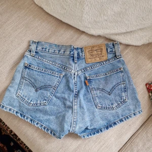 Levi's ljusblå jeansshorts - Klassiska ljusblå jeansshorts från Levi's med hög midja, fem fickor och knappgylf. Shortsens denim är i 100% bomull och har en avslappnad passform. Perfekta för varma dagar och en tidlös stil.