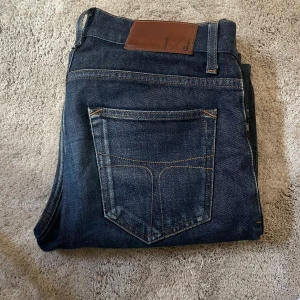 Mörkblå jeans tiger of sweden - Snygga mörkblå jeansbyxor från T/J med klassisk femficksdesign och kontrastsömmar. Byxorna har normal passform och raka ben. Perfekta till vardags och enkla att matcha med olika stilar.