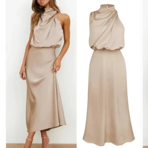 Champagnefärgad långklänning med draperad hals - Elegant långklänning i champagnefärgat satinmaterial med draperad, hög hals och ärmlös design. Klänningen har en figurnära passform upptill och faller snyggt längs kroppen. Perfekt för speciella tillfällen. Helt ny! Ej använd.