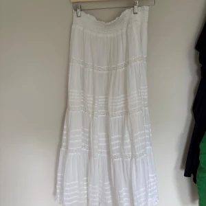 Vit långkjol från Neo Noir - Säljer en vit långkjol från Neo Noir i 100% hållbar bomull. Kjolen har smock i midjan och fina spetsdetaljer