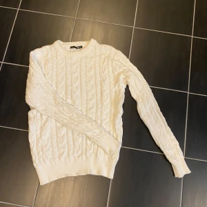 Vit kabelstickad tröja från 157 - Säljer en klassisk vit kabelstickad tröja från lager 157. Tröjan har rund halsringning, långa ärmar och ribbade muddar vid ärmslut och nederkant. Perfekt för lager-på-lager och enkel att matcha med olika outfits. I fint skick!