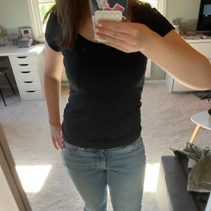 Svart t-shirt med rund hals - En klassisk svart t-shirt med rund hals och korta ärmar. T-shirten har en normal passform och är tillverkad i ett mjukt bomullsmaterial. Perfekt basplagg att matcha med jeans eller kjol.