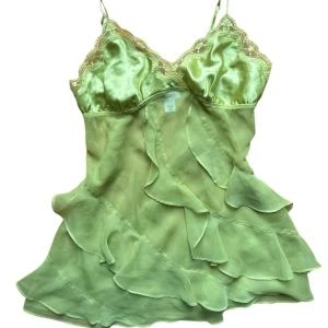 Ljusgrön volangig satinlinnetopp från La Senza - Säljer en ljusgrön linnetopp från La Senza i satin med tunna axelband, spetsdetaljer vid bysten och volanger framtill. 
