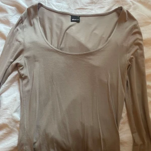 Beige långärmad topp från Gina Tricot - Säljer en enkel och stilren beige långärmad topp från Gina Tricot. Toppen har en rund, djup ringning och är gjord i ett mjukt bomullsliknande material. 