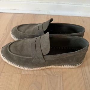 Olivgröna mocka loafers med flätad sula - Snygga olivgröna loafers i mocka med klassisk design och flätad sula i espadrillestil. Skorna har rund tå och en stilren ovandel utan snörning, perfekta för en avslappnad men trendig look. Dm för frågor, priset kan diskuteras!