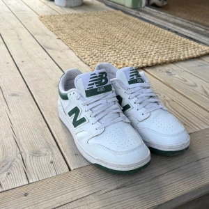 Vita New Balance 480 sneakers med gröna detaljer - Säljer ett par fräscha vita New Balance 480 sneakers som använts fåtal gånger med gröna detaljer och klassisk N-logga på sidan. Skorna har snörning, perforerad tå och platt sula. Perfekta för en sportig och stilren look. Nypris 1250kr