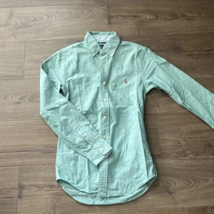 Ljusgrön skjorta från Ralph Lauren - Säljer en ljusgrön skjorta från Ralph Lauren i slim fit-modell. Skjortan har klassisk krage, knappar framtill och broderad logga på bröstet. Perfekt för dig som gillar stilrena och tidlösa plagg. Använd men väldigt bra skick, pris kan diskuteras vid snabb affär
