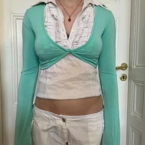 Mintgrön bolero med lång ärm - Superfin mintgrön bolero med lång ärm och knapp framtill. Sitter tajt och har en snygg, enkel design som passar perfekt över linne eller topp. Tunn och mjuk i materialet, perfekt för lager-på-lager-stil.