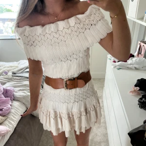 Offshoulder vit kortklänning med volang - Superfin offshoulder kortklänning i vit med volangkant och broderade detaljer. Klänningen har en luftig passform, markerad midja med bredt bälte och plisserad kjol med volanger. Man får med bältet men man kan också ha klänningen utan bältet☺️❤️