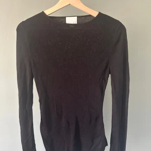 Svart långärmad stickad tröja - En svart, tunnstickad långärmad tröja med rund halsringning. Tröjan har en slim passform och är perfekt att styla med jeans eller kjol. Enkel och stilren design som funkar till många olika looks.